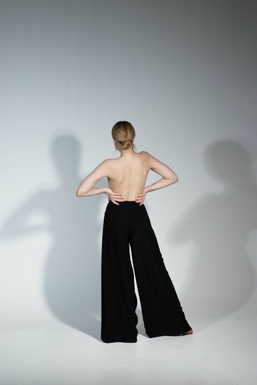 shirtless woman in wide pants casting shadows on wall