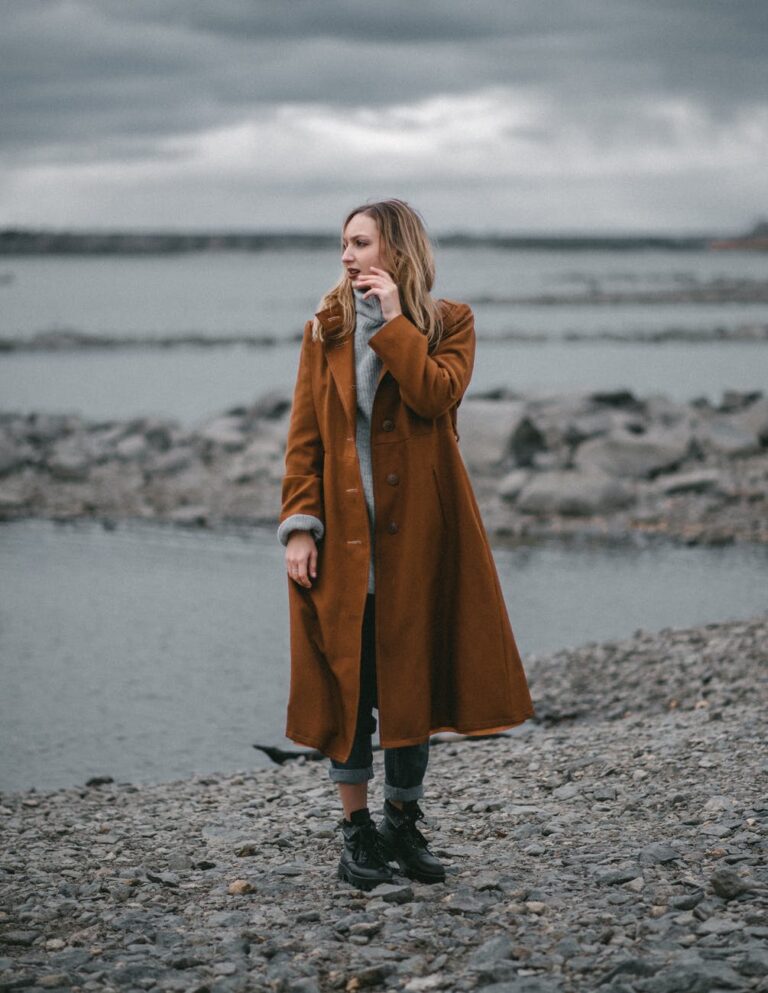 woman in trendy long beige coat on coast of sea