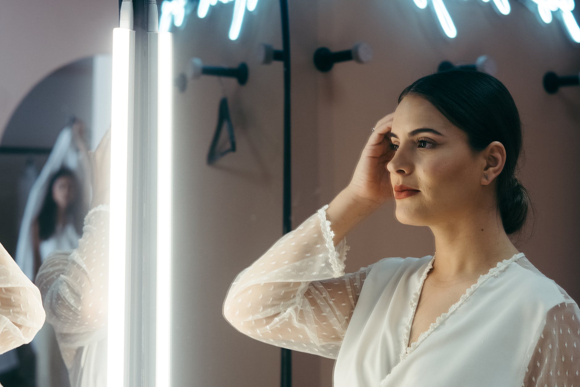 a woman in white blouse looking at her own reflection on the mirror